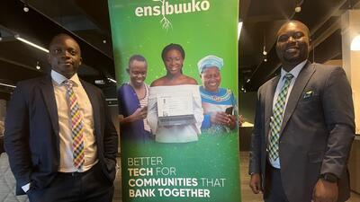 Two Ugandan businessmen standing next to green banner reading Ensibuuko