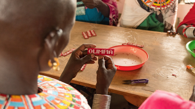 Close-up of Kenyan woman designing beadwork that reads Olimpia