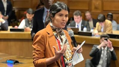 Woman in brown jacket stands to speak at UN forum