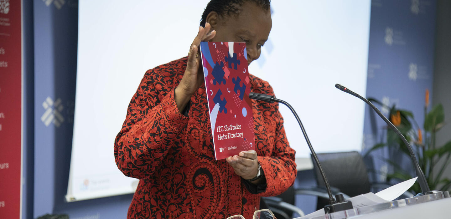 Mujer de pie detrás de un podio sosteniendo un folleto.