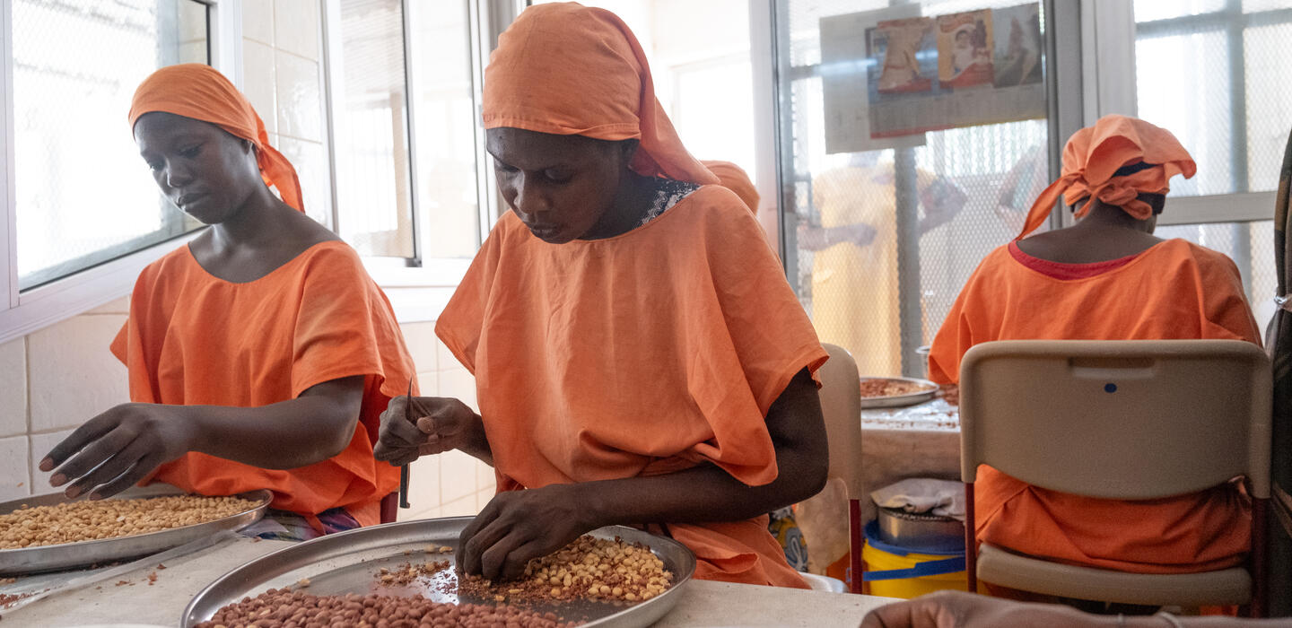 Women in orange uniforms work cashews into snacks