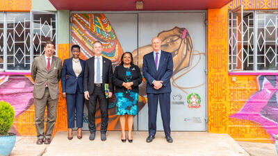 Officials in business attire stand by a wall with a brightly coloured mural