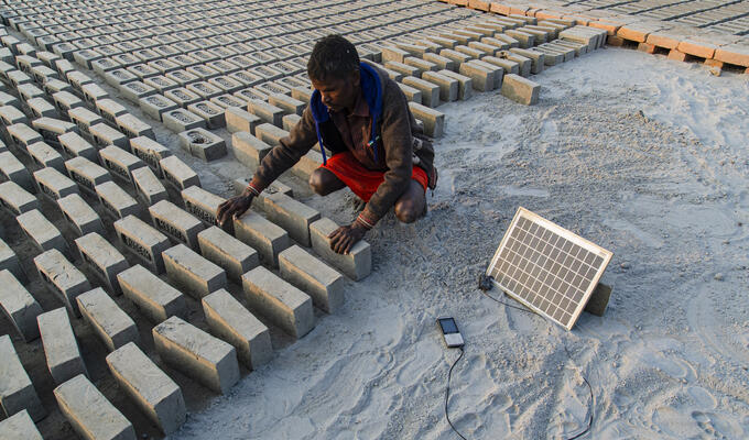 A brick worker charges his phone using a portable solar panel in a brick factory in West Bengal, India