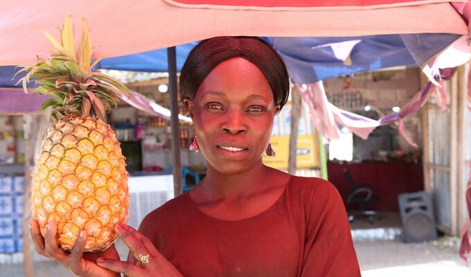 South Sudanese farmer holds pineapple at market stall in Juba