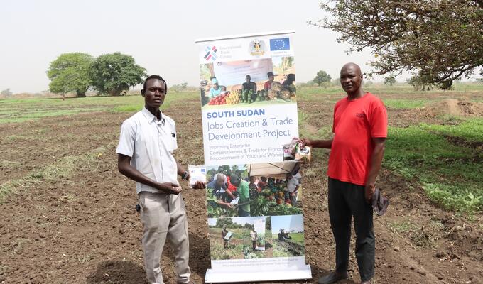 two south sudanese farmers stand next to banner in field