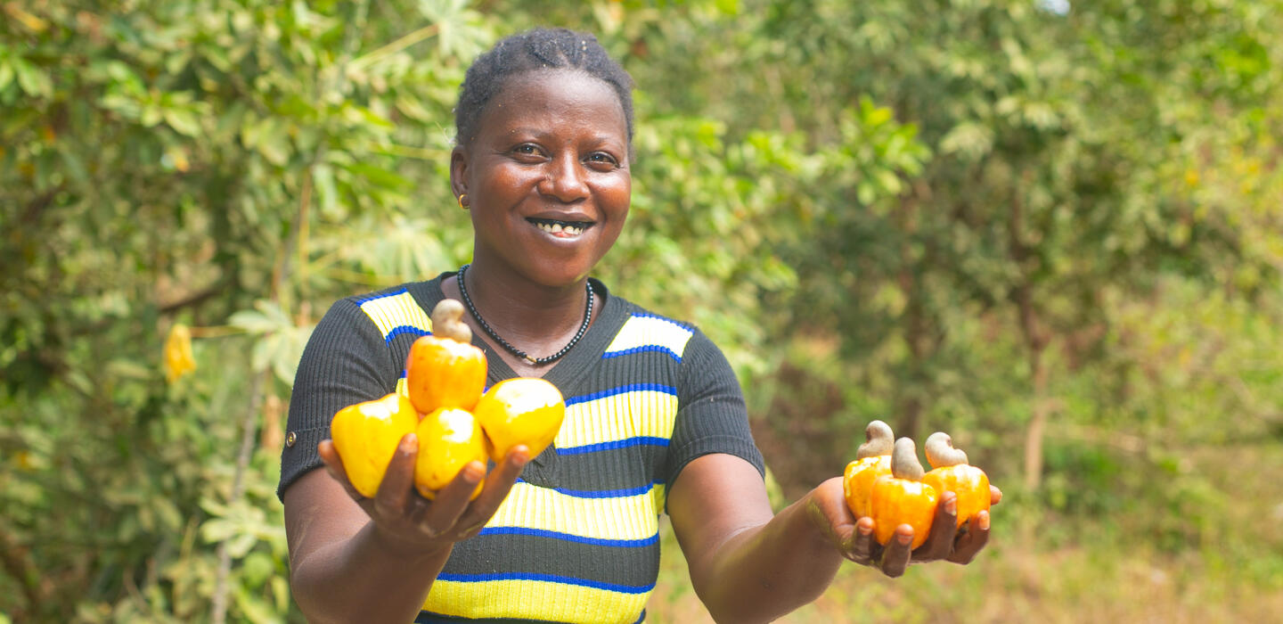 Woman farmer smiling and holding cashew fruits in both hands.
