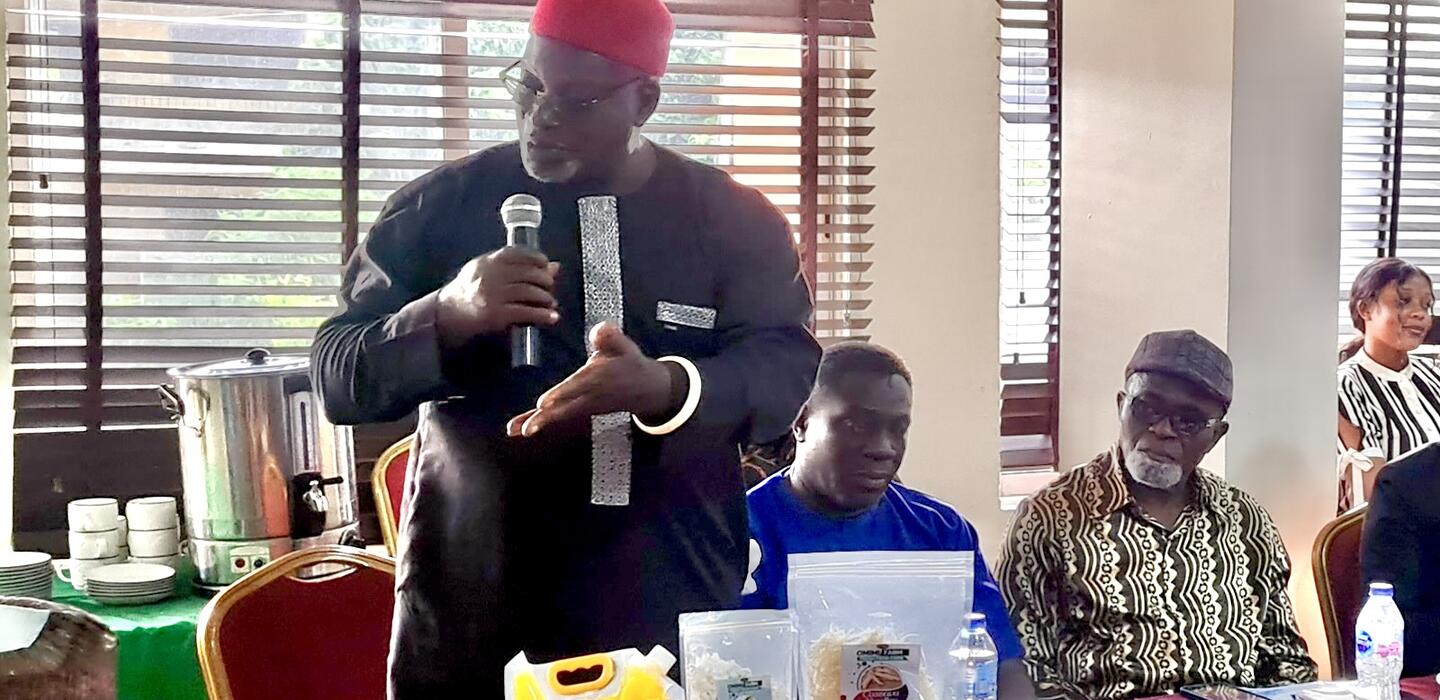 Nigeria man stands with microphone behind three samples of local food products
