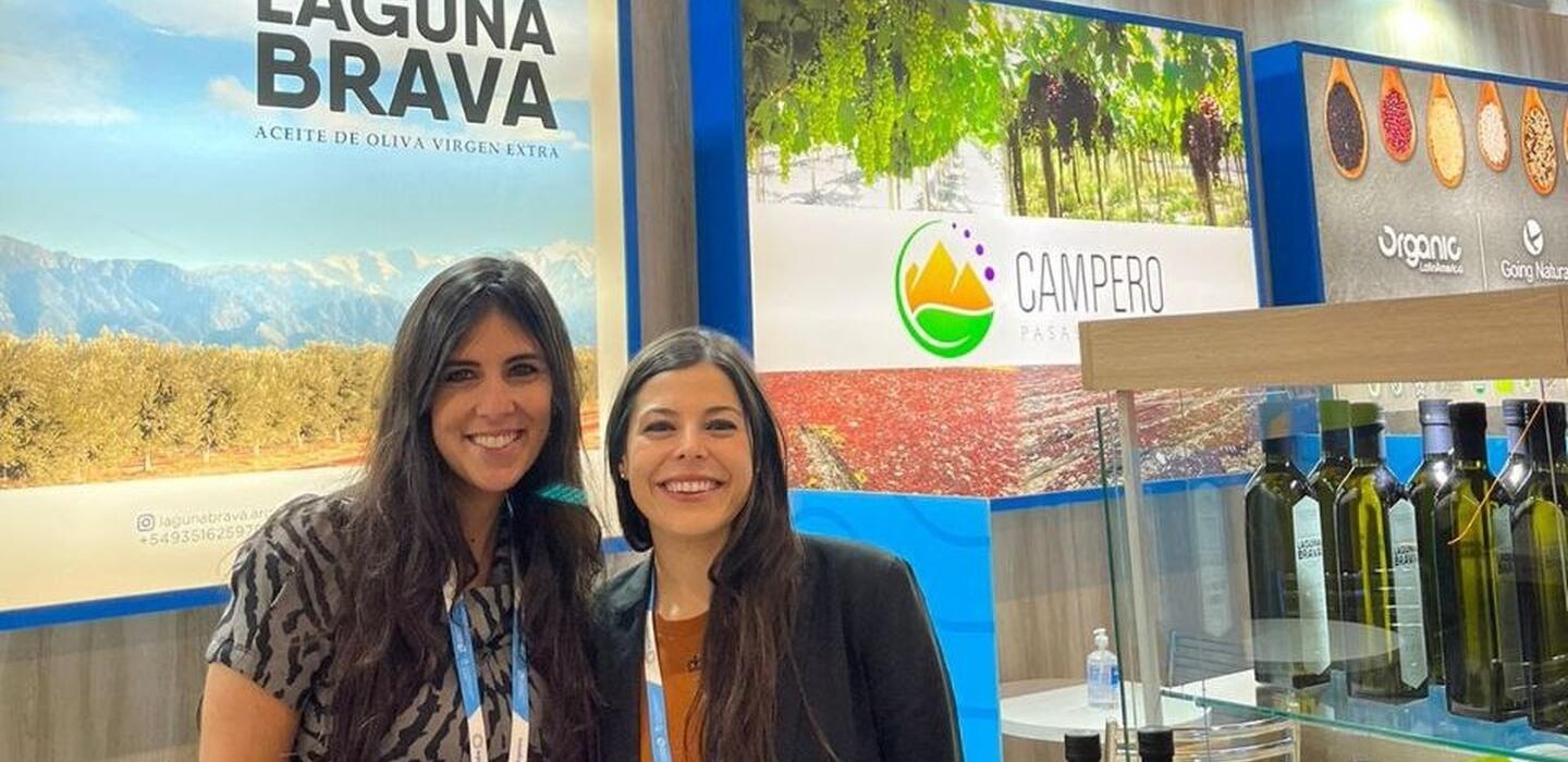 Two Argentine women stand in front of sign for olive oil, with samples nearby in glass case