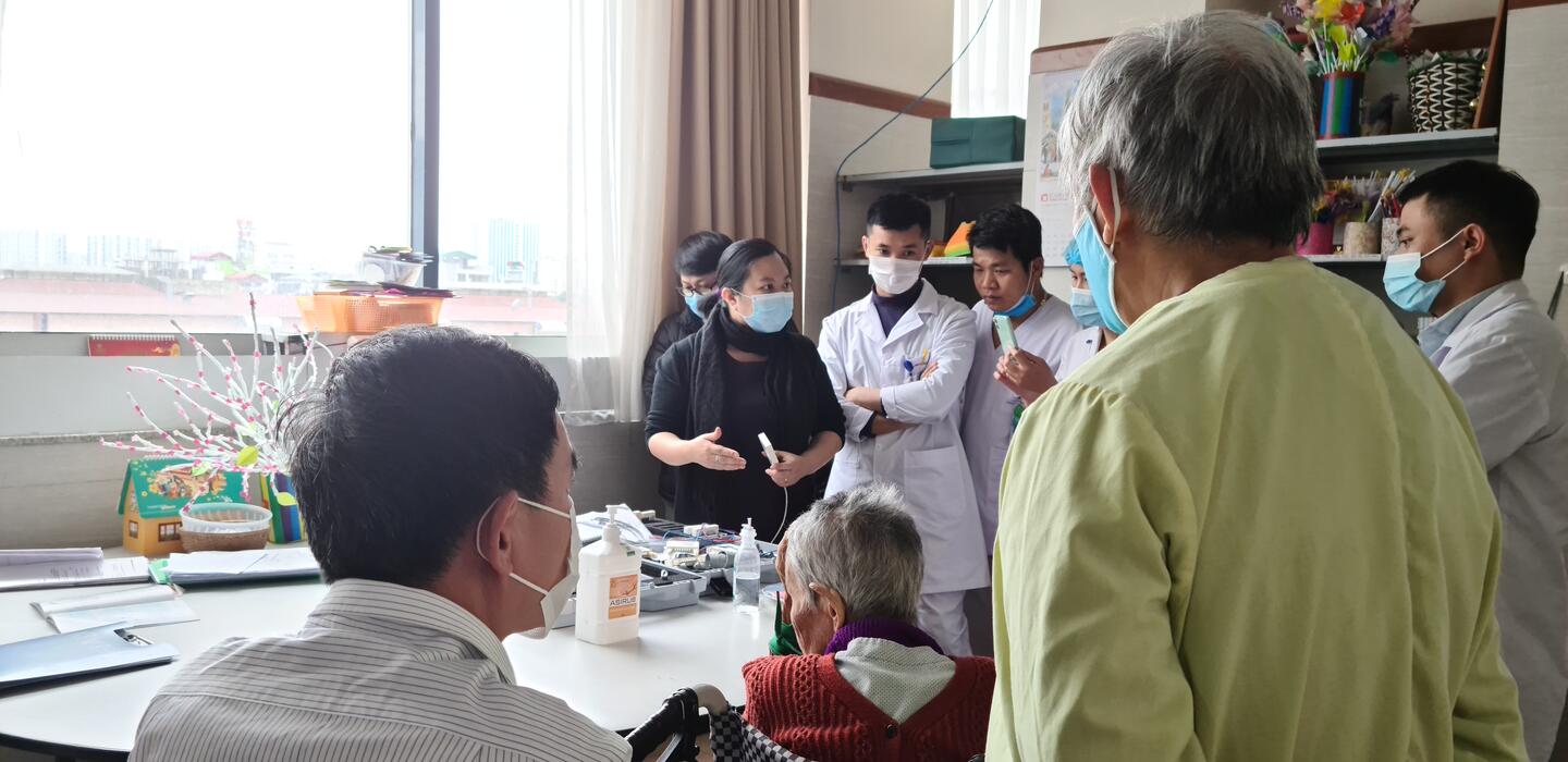 Woman shows medical equipment to group standing around a table