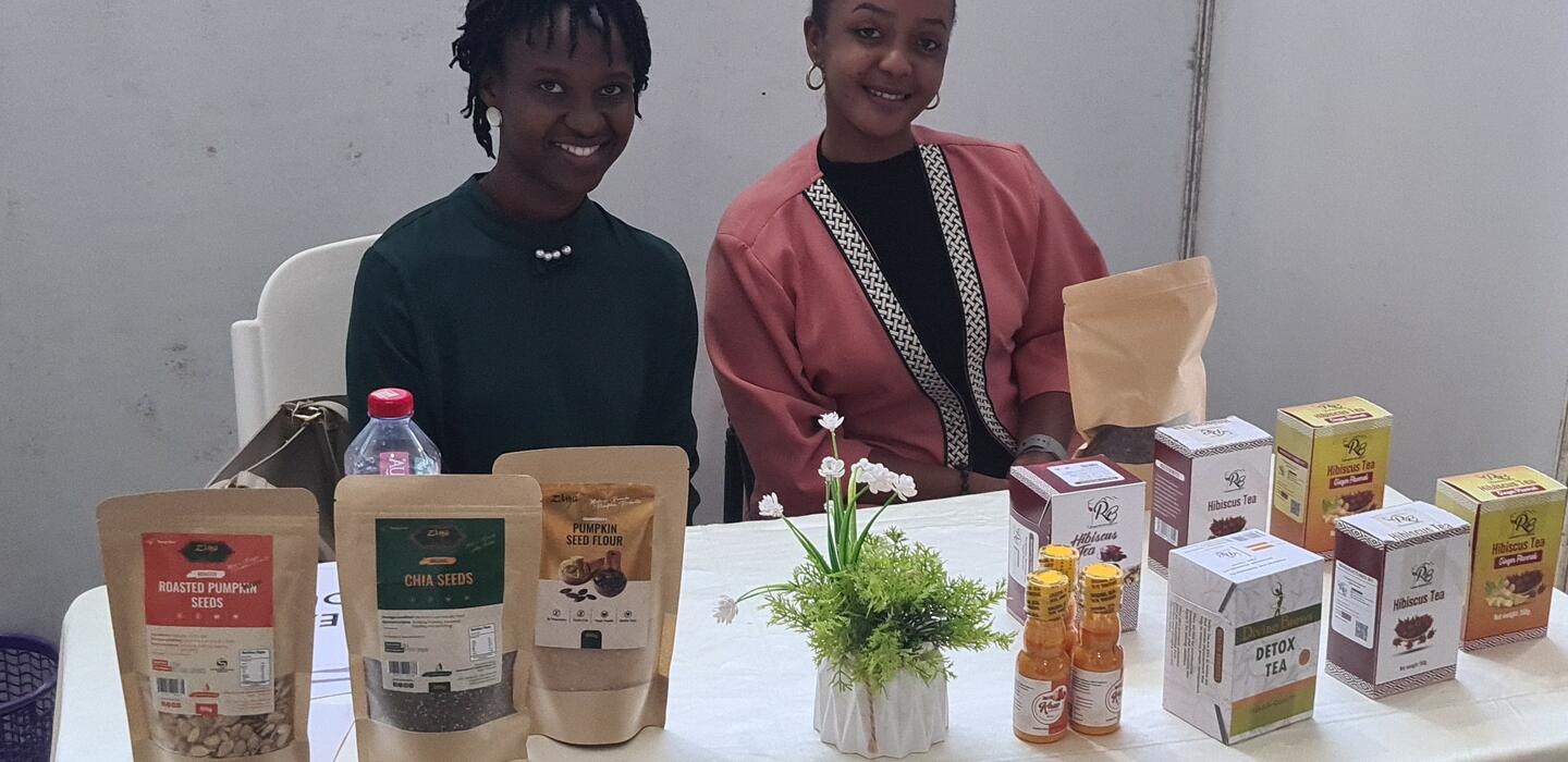Two Rwandan women sitting behind a table displaying dried seeds and tea products.  